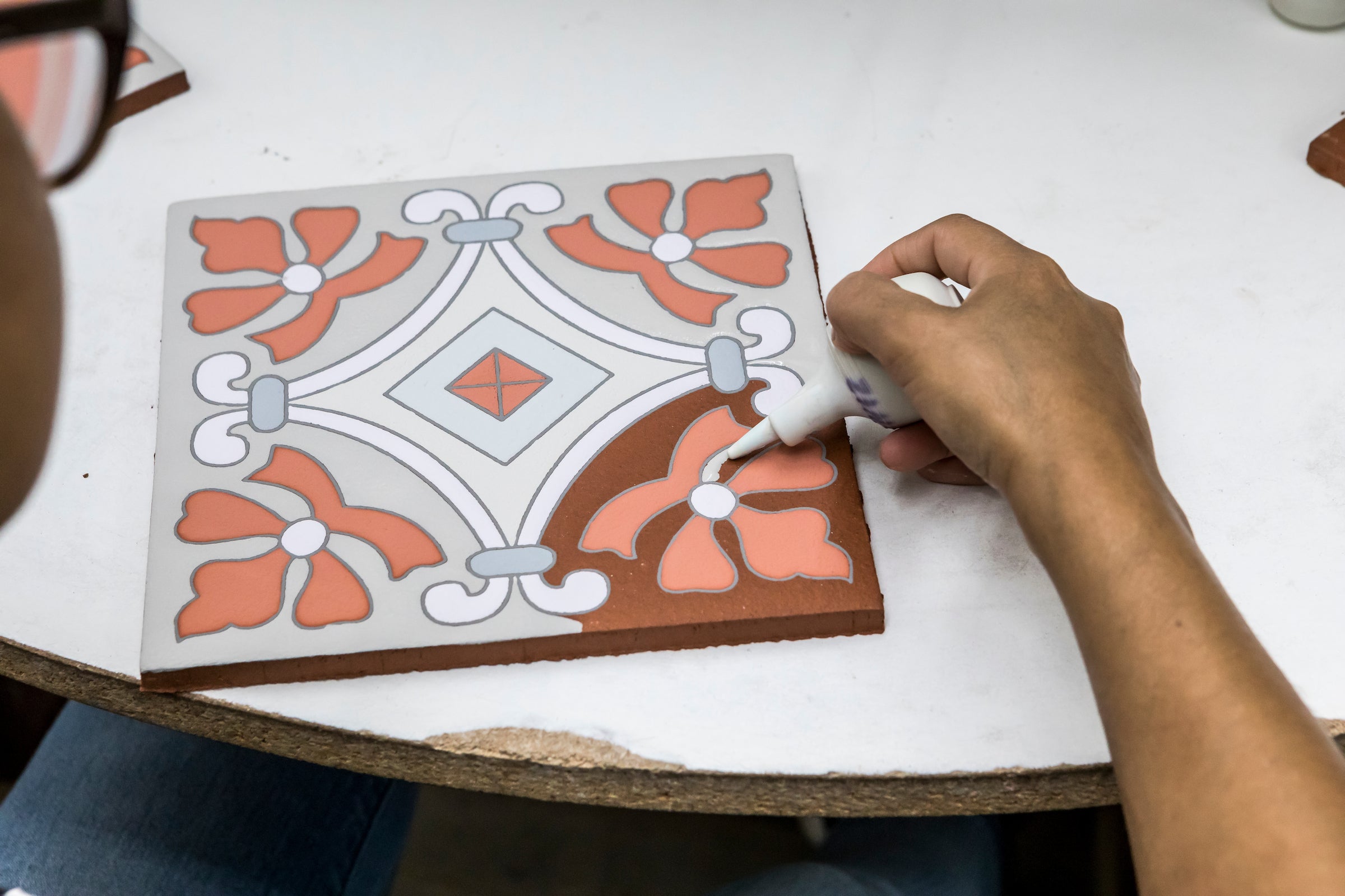 A maker hand-glazing a patterned tile, line by line
