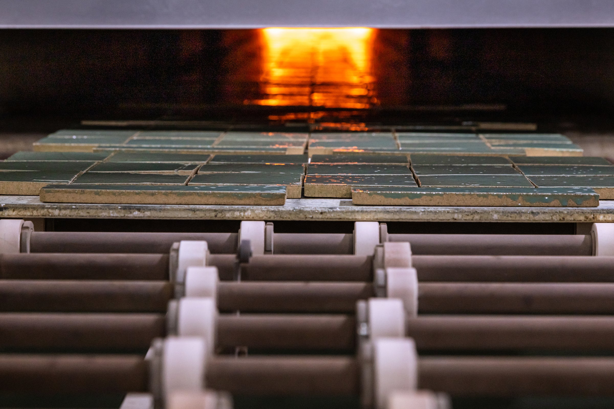 Glazed green clay tile rolling into the glowing kiln