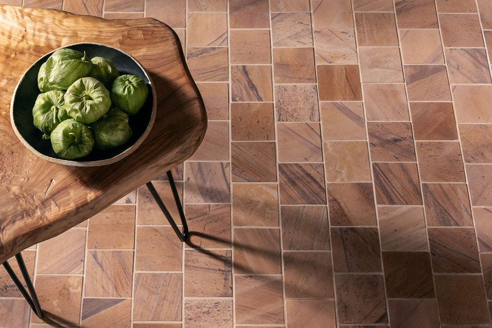 A floor of Stone Born quartzite laid in mixed sizes, tan, pink and grey pieces with dark veining, with a live edge side table on it holding a bowl of tomatillos