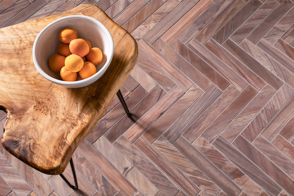 A herringbone floor of long Stone Born quartzite pieces in pink, mauve and tan with sweeping veins, with a live edge side table on it holding a white bowl of apricots