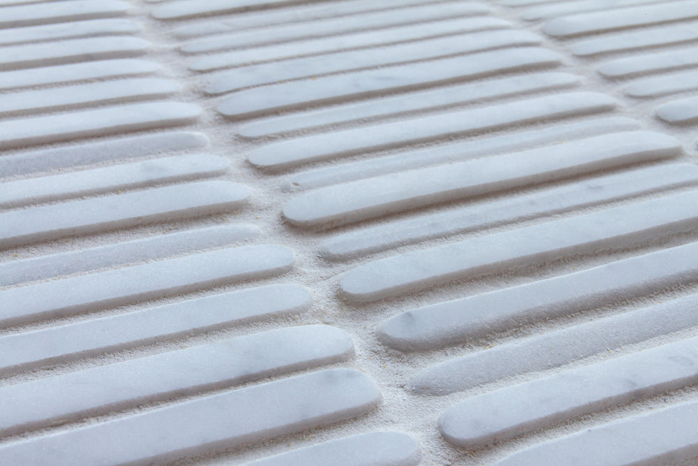 Narrow rectangular marble pieces laid in offset rows and seen at an angle, pale grey and white with softly rounded edges